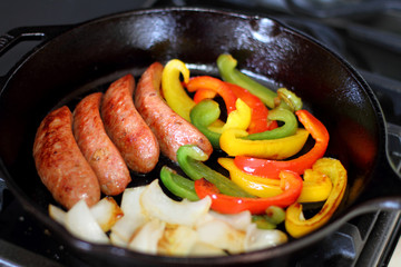 Sausage cooking on the stove in a cast iron skillet with bell peppers and onion.