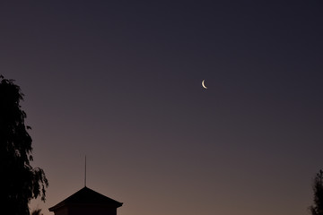 Incipiente luna cuarto creciente sobre los edificios al atardecer