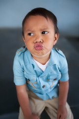 A boy looking away with lips puckered up with a moody expression while sitting down.