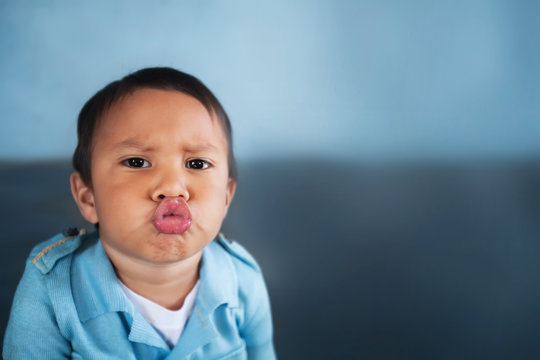 Young boy puckering up his lips to give a kiss and wearing a light blue vintage shirt.