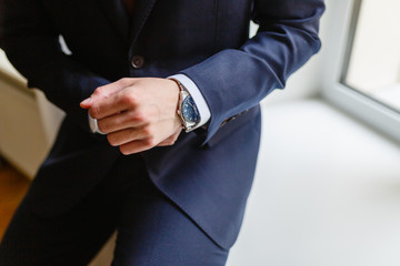 Close-up of a man in an expensive tailored suit straightens shirt cuffs. Man sitting on the windowsill by the window