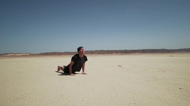 Attractive male doing yoga sun greeting suria namaskar on a rock in desert