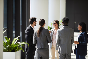 Positive business team in formalwear standing in circle in modern lobby and discussing ideas for...