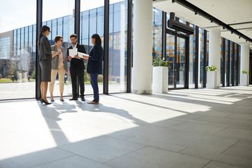 Group of creative interracial business people in formal outfits standing near panoramic window and...