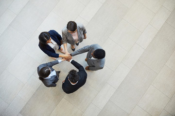 High angle view of multi-ethnic business people standing in circle and stacking hands while supporting each other, team motivation concept