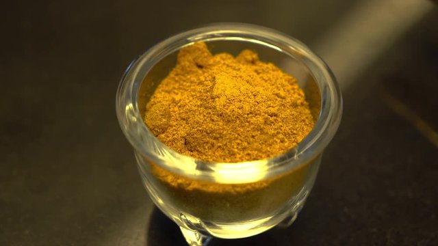A steady, extreme close up shot of a tiny glass bowl filled with an orange powdery condiment.