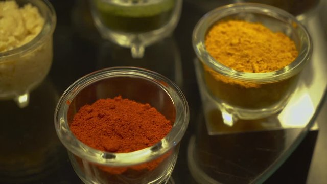 A steady, extreme close up shot of small bowls filled with some orange and red condiments.