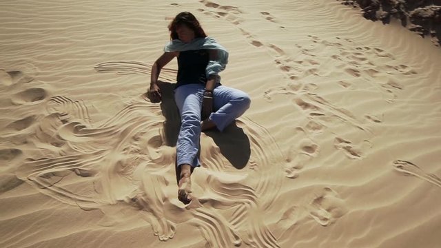Handsome smiling female extatic dancing on sand dune in desert slow motion