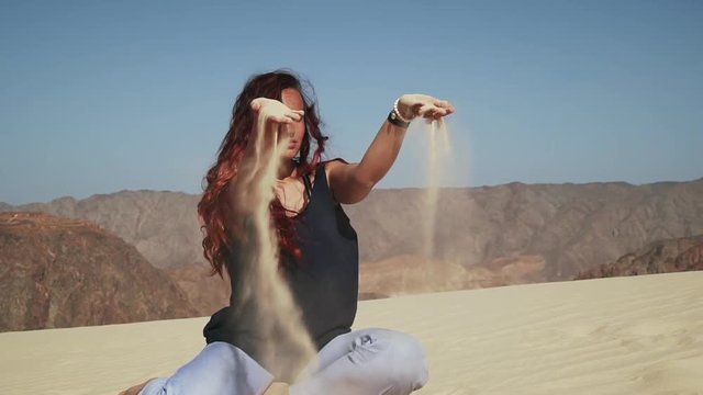Attractive smiling female extatic dancing on sand dune in desert slow motion