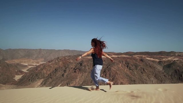 Handsome female extatic running on sand dune in desert slow motion
