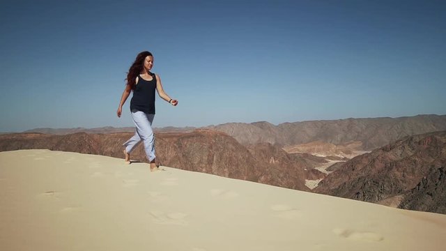 Handsome female extatic running on sand dune in desert slow motion