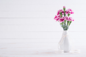 Valentines day and love concept. Pink carnation flower in vase on white wooden background.