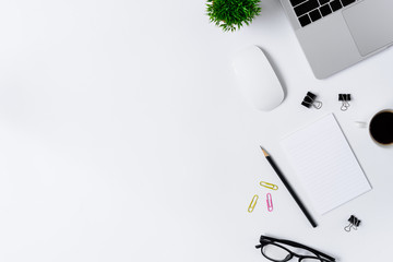 The office desk flat lay view with laptop, mouse, tree, pink and yellow paper clip, coffee cup, notebook, pencil, black glasses on white background.