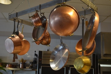 Copper kitchen cookware on an overhead rack.