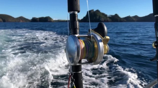 SLOW MOTION - Close up shot of fishing rod and overhead reel on sunny blue sky day with island and rocks in the background