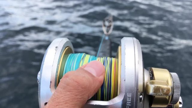 Fingers on reel letting line run color braided line close up shot