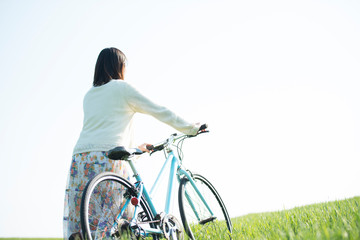 Obraz premium 草原で自転車を押す女性の後姿