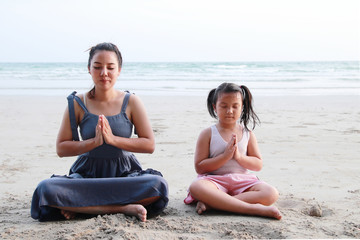 Mom is teaching child to do meditation on the beach