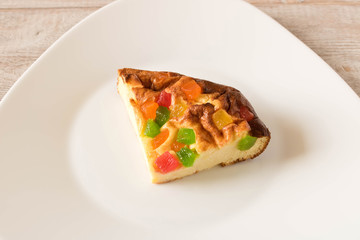 A piece of cottage cheese casserole with candied fruits on a white plate. Close up.