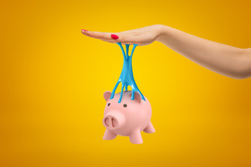 Pink piggy bank stuck to female hand with blue sticky slime on yellow background