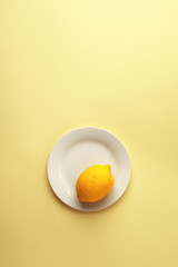 Creative monochrome summer layout made of lemon on white plate on yellow background. Fruit minimal concept.