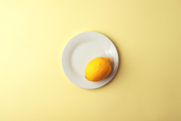 Creative monochrome summer layout made of lemon on white plate on yellow background. Fruit minimal concept.