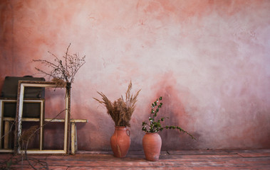 Empty frames, clay jugs with branches on the background of the wall. Vintage style interior...