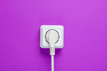 White cable plugged into power outlet on a purple wall background