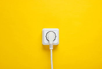 White cable plugged into power outlet on yellow wall background