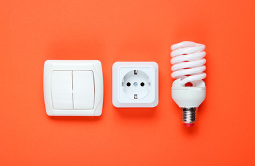 Economy spiral light bulb, electric plug, switch on orange background. Top view. Minimalism electro consumer concept