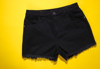 Fashionable women's denim black shorts on yellow background. Top view