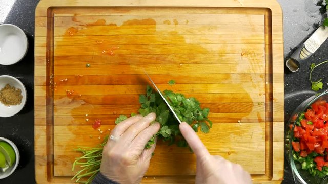 Overhead shot of chopping green cilantro on a wood cutting board.