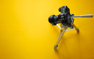 Modern digital camera with tripod on  yellow background. Minimalism. Top view