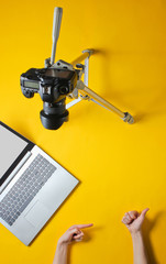 Obraz premium Blog minimal concept. Like and subscription. Female hands are blogging with camera on tripod and laptop on yellow background. Top view