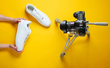 Women reviews new white sneakers with camera on tripod on yellow background. Top view. Minimalism