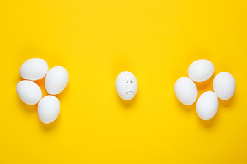 Bullying concept with eggs on yellow background. Top view, minimalism