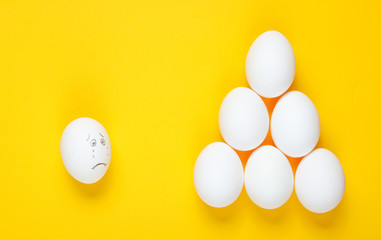 Bullying concept with eggs on yellow background. Top view, minimalism