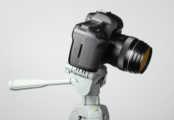 Modern digital camera with a tripod on gray background