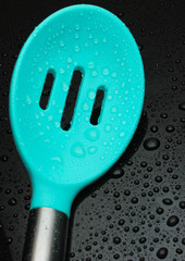 Silicone kitchen spoon colander in water drops on black background