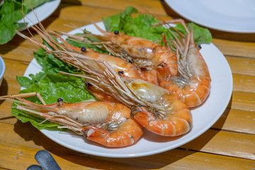 Freshly burned shrimp In a tile dish on a bamboo table and with fresh vegetables