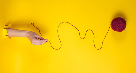 Female hand holding skein of thread through torn yellow paper. Minimalistic creative medicine concept