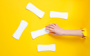 Female hand holds daily sanitary pad through torn yellow paper background. Minimalistic fashion concept