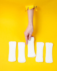 Female hand holds daily sanitary pad through torn yellow paper background. Minimalistic fashion concept