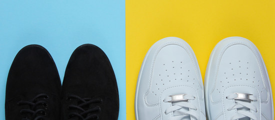 White fashionable sneakers and black suede shoes on a blue-yellow background. Top view.