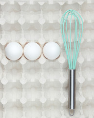 Whisk and eggs in tray. Top view, closeup
