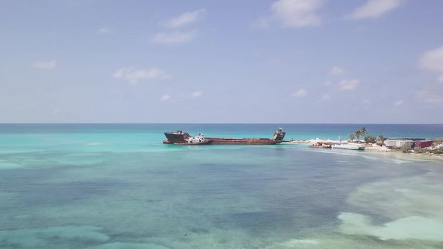 Aerial shot getting closer to an abandoned ship on an Island in Bahamas with blue water.