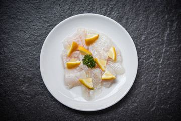 Fresh raw fish fillet piece on white plate with lemon on dark background - pangasius dolly fish meat