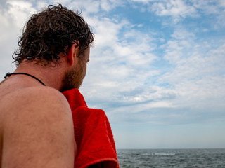 a man with a beard wipes off a towel after swimming in the sea.back view