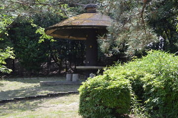 陽射しを浴びた庭木と、日陰をつくる東屋がある日本庭園の風景