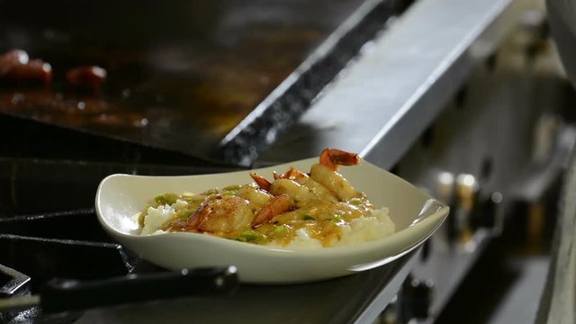 Chef placing shrimp and sausage on a bowl of shrimp and grits
